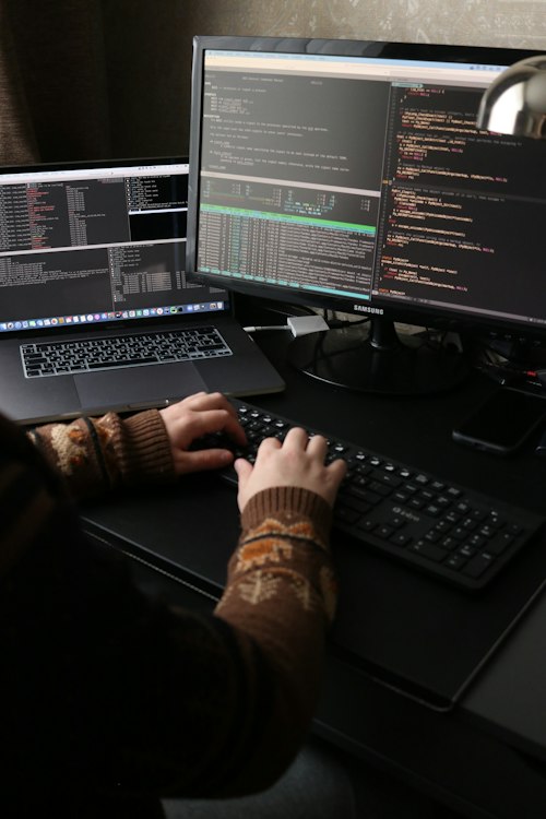 Mains sur un clavier devant des écrans de code